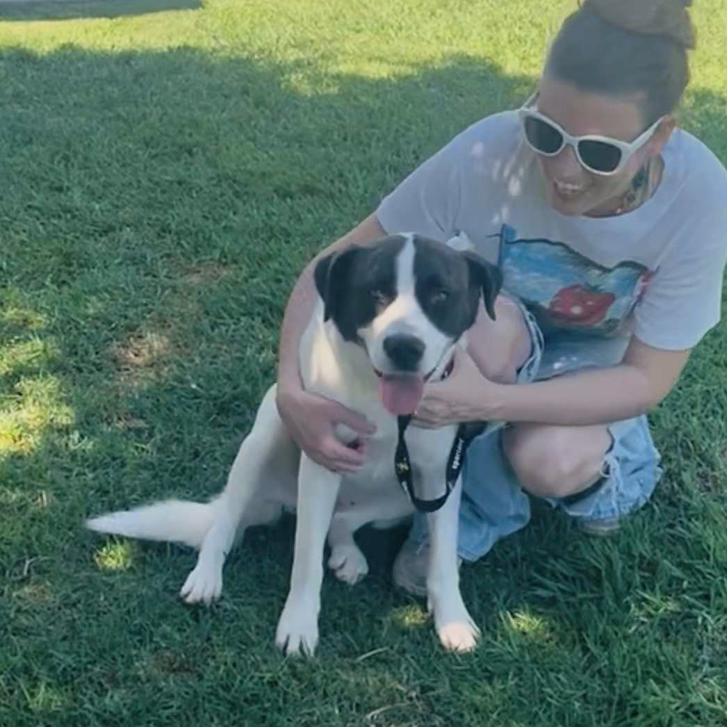 Dolly sitting beside a caregiver on the grass, with the caregiver’s arms around her.